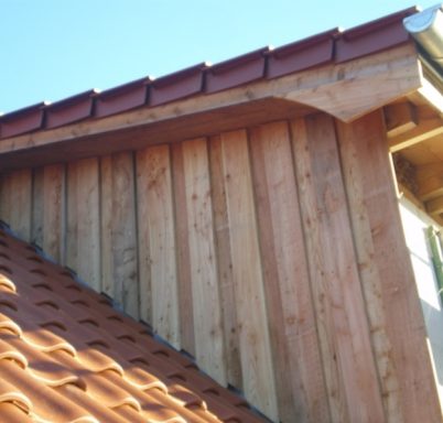 Holzverkleidung und Ziegeldach eines Gebäudes unter blauem Himmel.